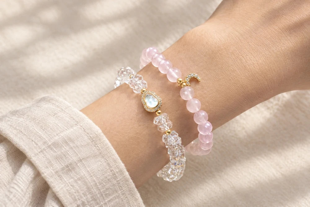Rose quartz and clear quartz bracelets stacked on a wrist, with gold-tone accents and a crescent moon charm.