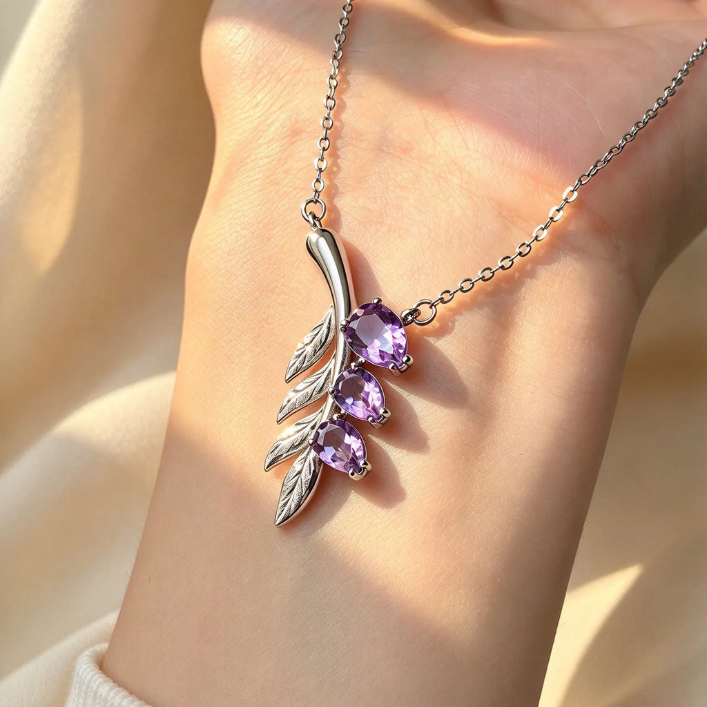 Lavender Sprig necklace with three purple amethyst stones and a silver-tone leafy pendant held against a palm.