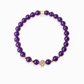 Close-up detail of sparkling pave crystal lucky clover pendant and golden mantra spacer bead on deep purple amethyst mantra bracelet
