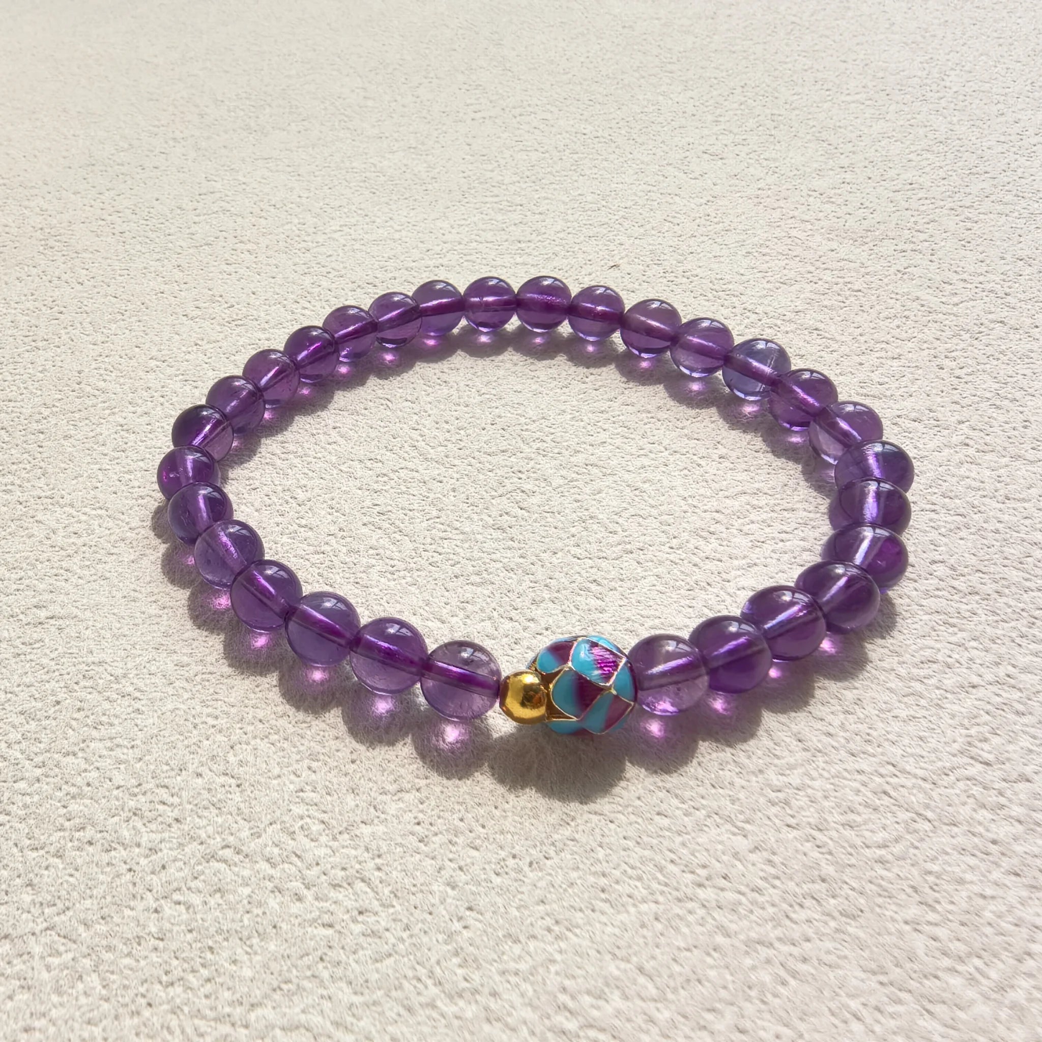 Close-up shot of vibrant multicolor enamel lotus bloom focal bead on translucent deep purple amethyst crystal bracelet
