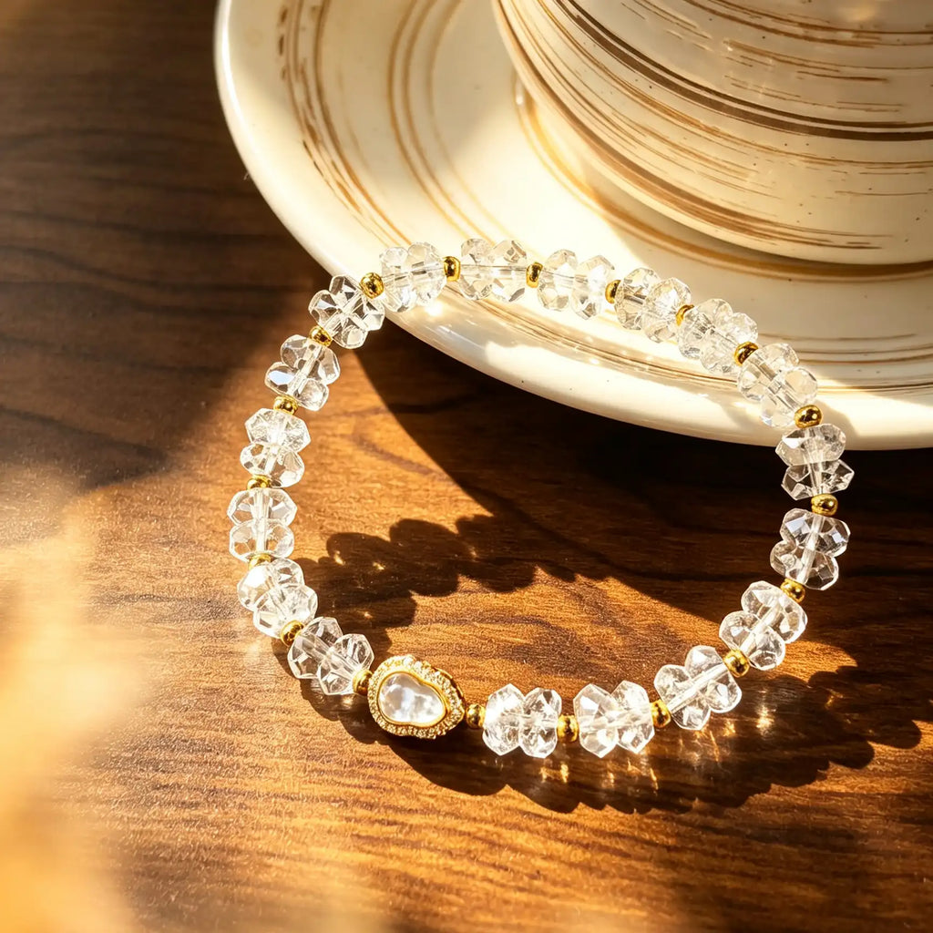 Faceted clear quartz bracelet with a gold-tone pear shaped centerpiece lying on a wooden desk beside a coffee cup.