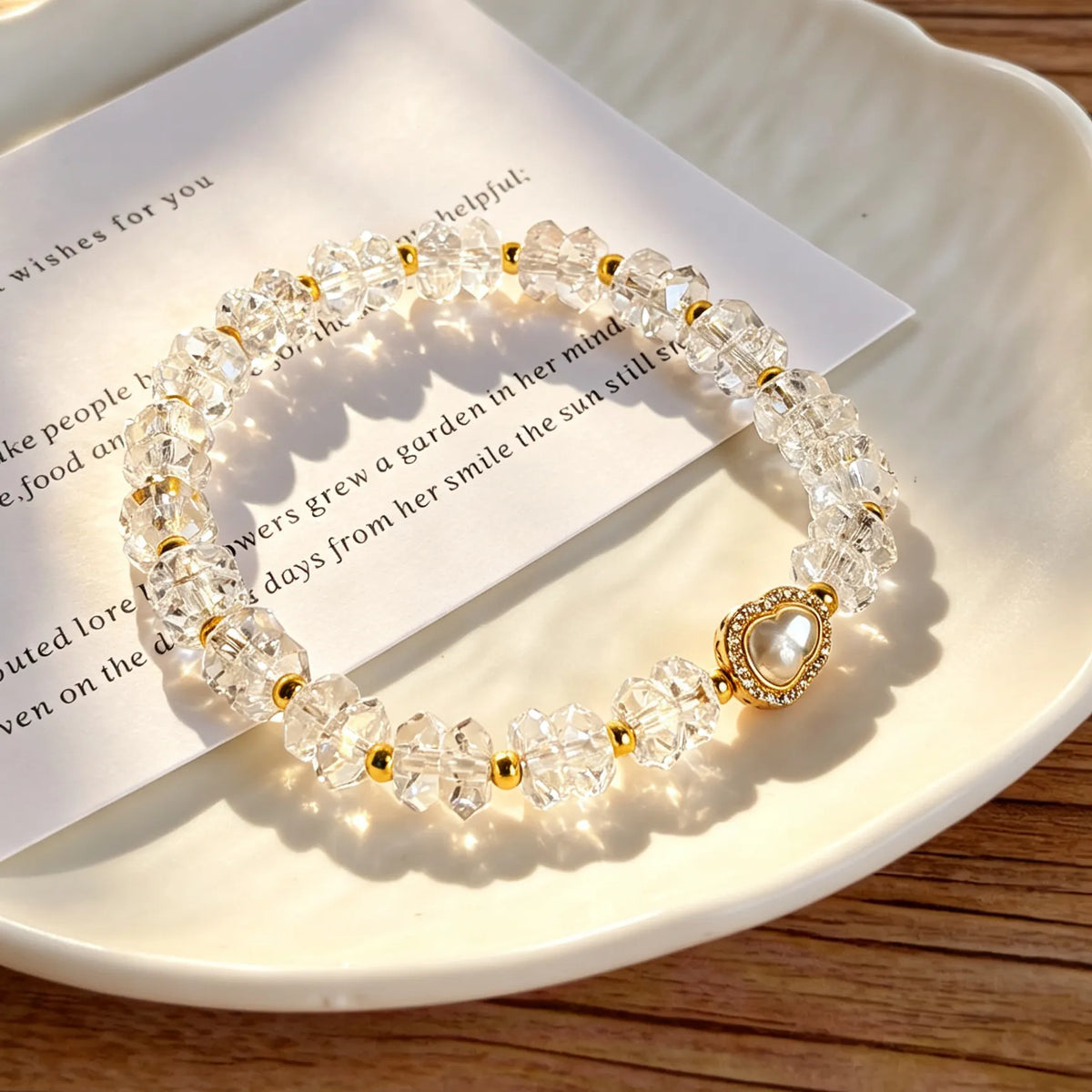 Faceted clear quartz bracelet with a gold-tone pear-shaped centerpiece lying on a plate and card.