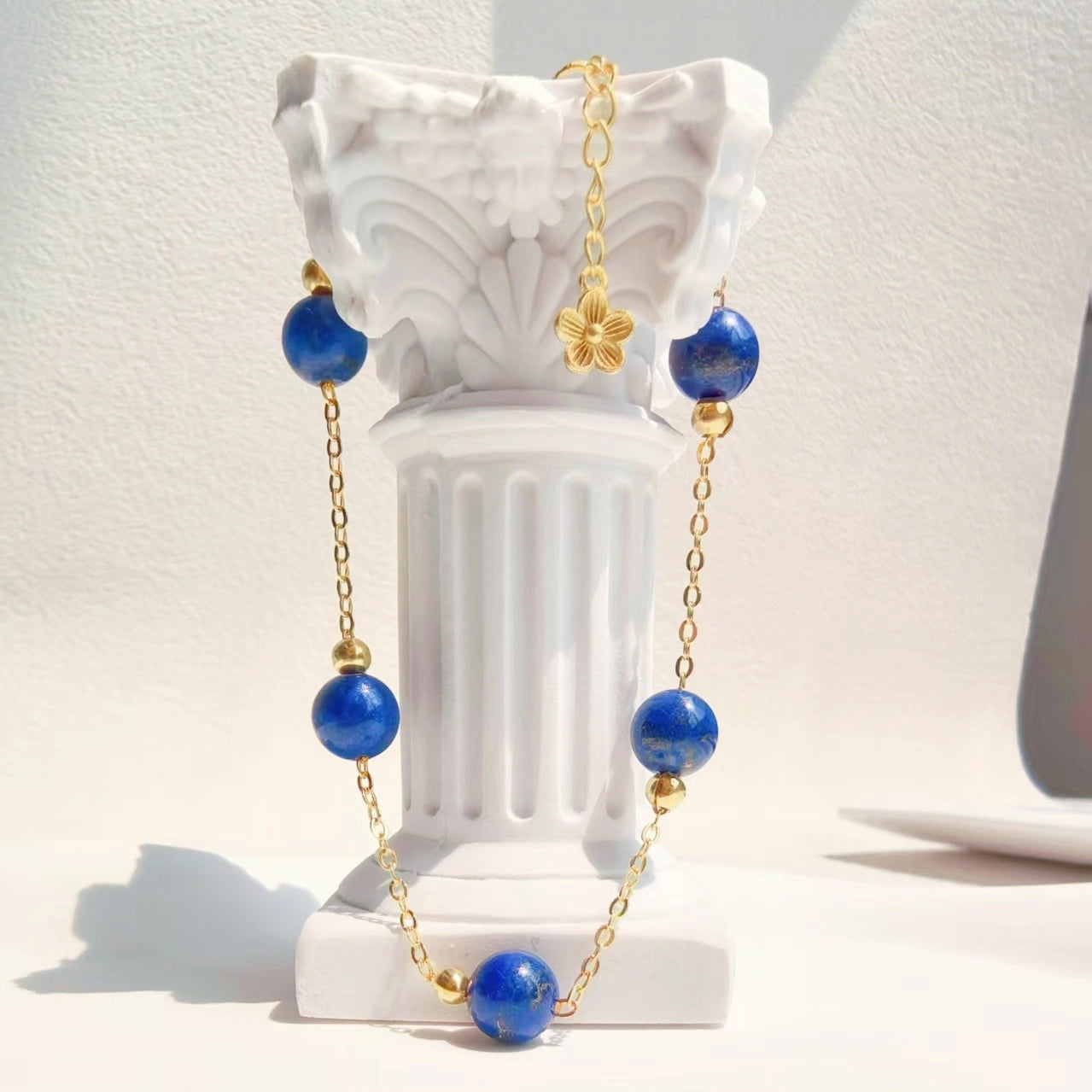 Close-up of delicate gold four leaf clover charm and adjustable extension chain on Milky Way Stroll Lapis Lazuli Bracelet，throat chakra crystal jewelry。
