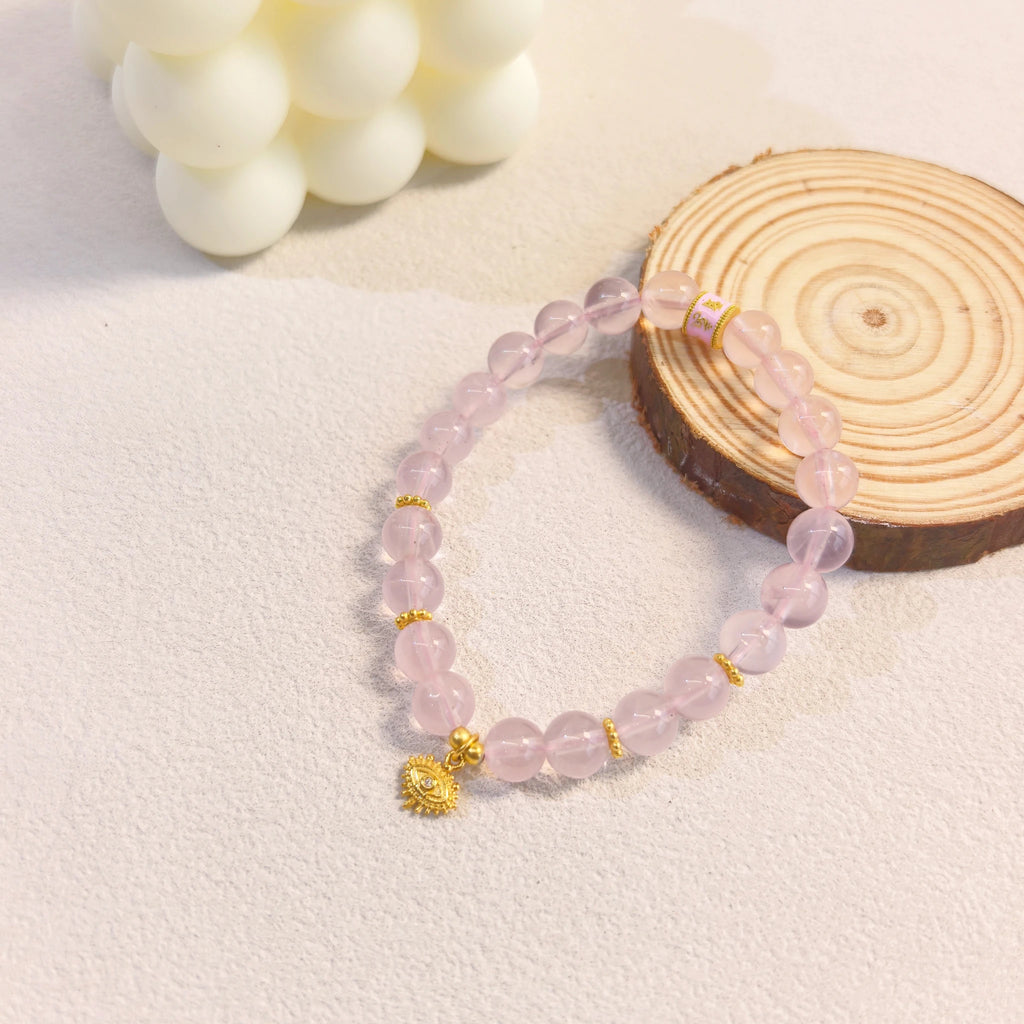 Cozy ins still life styling of pink aura evil eye protection crystal bracelet with wood and cream candles, healing crystal for heart chakra