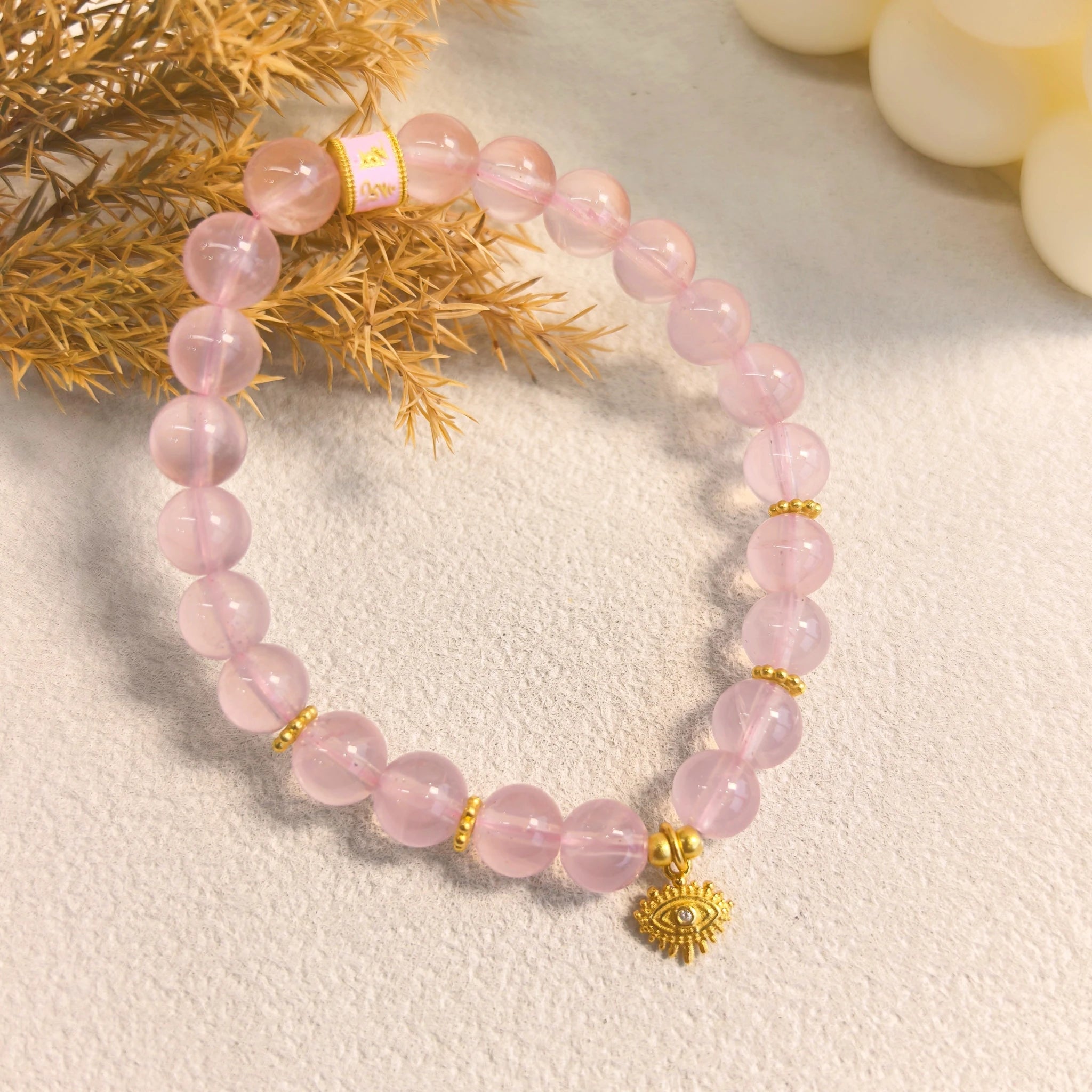 Cozy ins still life styling of pink aura evil eye protection crystal bracelet with dried grass and cream candles, witchy feminine spiritual jewelry decor