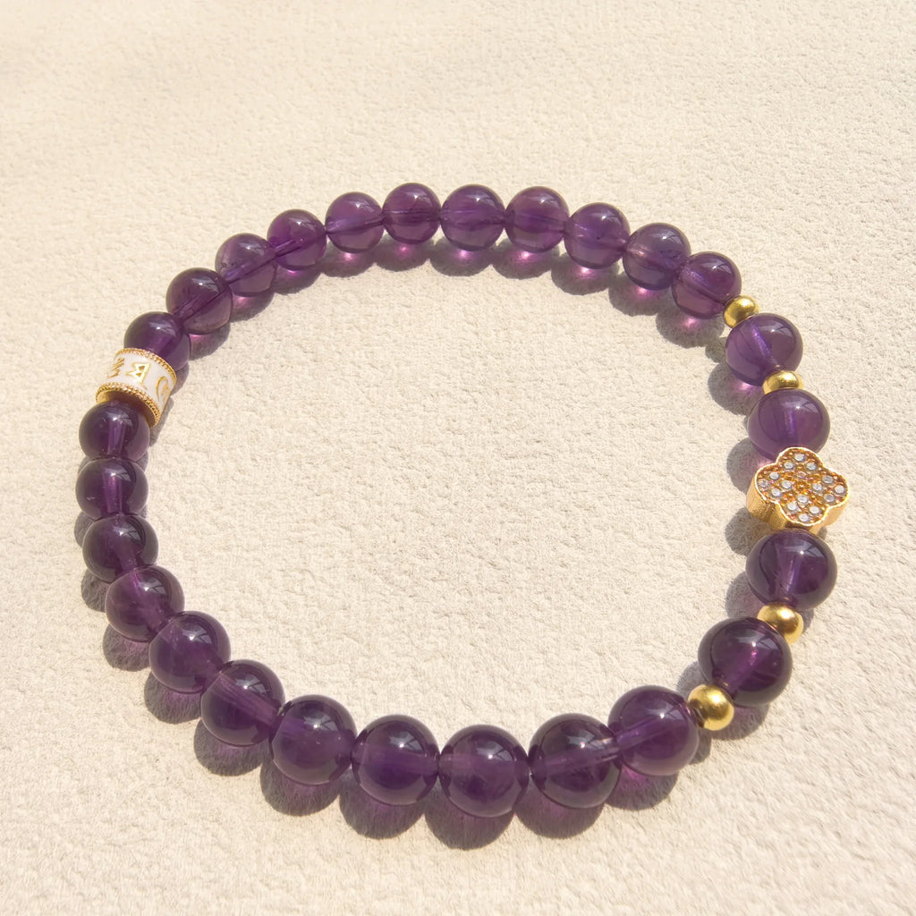 Close-up detail of sparkling pave crystal lucky clover pendant and golden mantra spacer bead on deep purple amethyst mantra bracelet