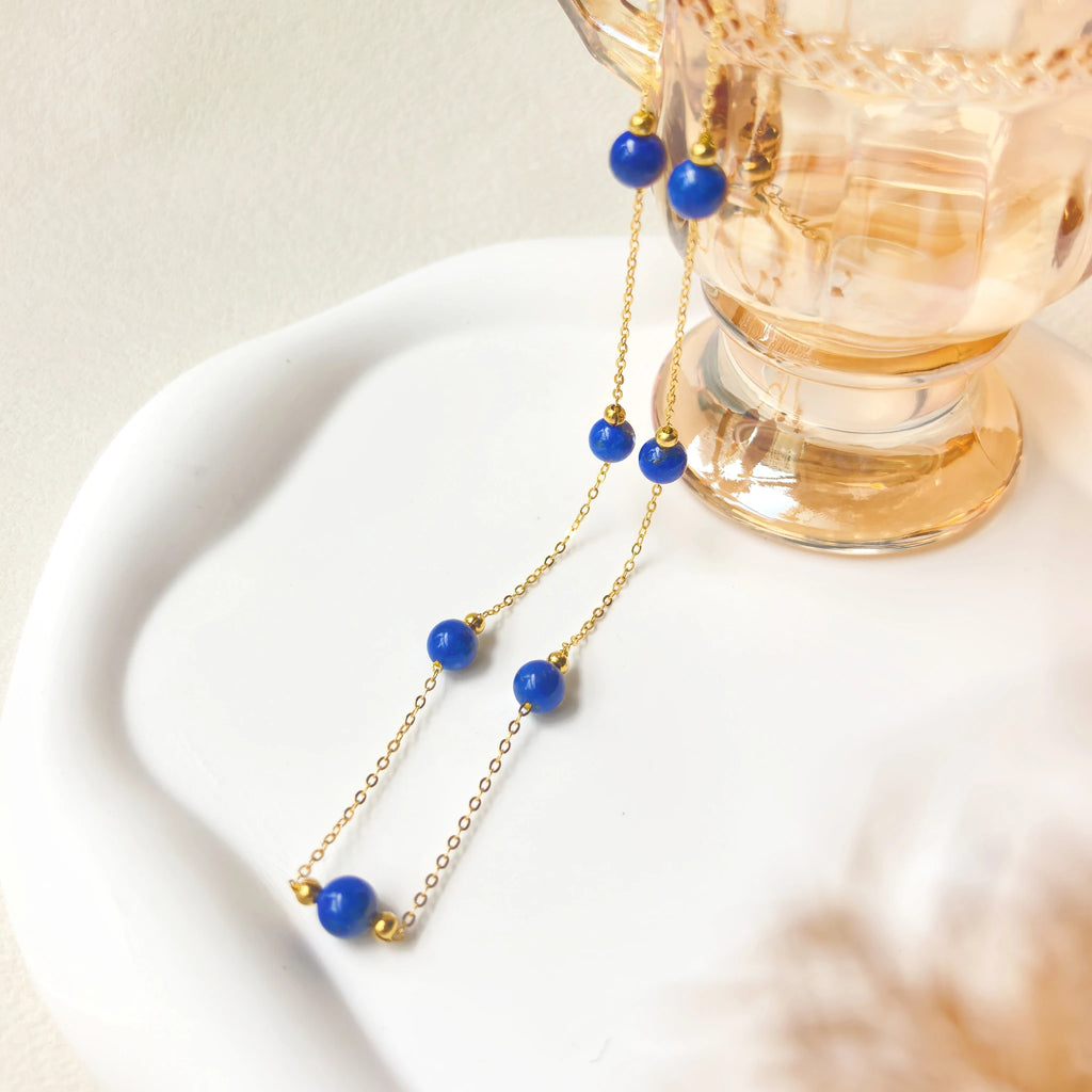 Close up of polished natural lapis lazuli bead on thin gold chain, milky way stroll gem necklace texture detail