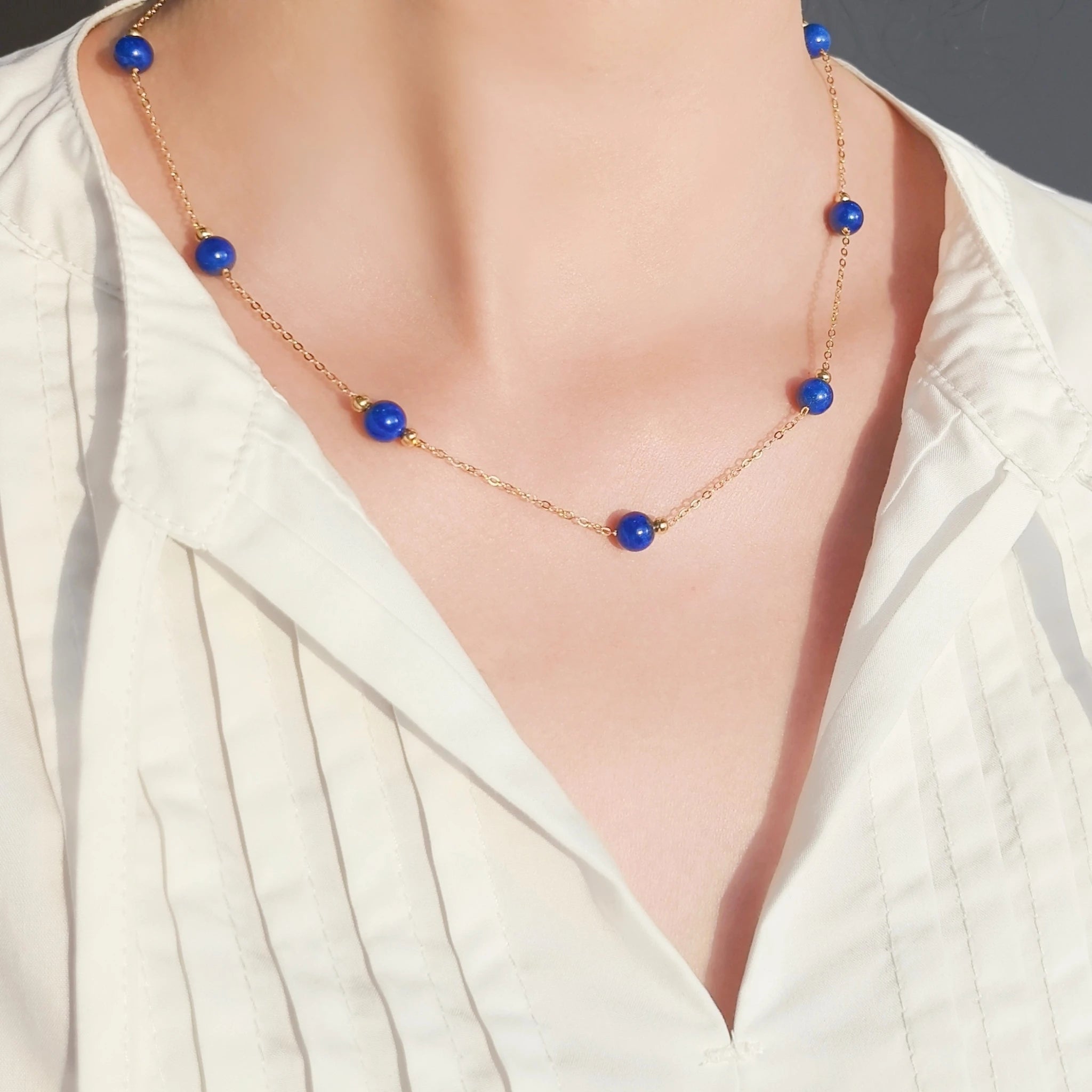 Woman wearing Milky Way Stroll lapis lazuli gold necklace with white blouse, healing lapis bead chain for daily wear.