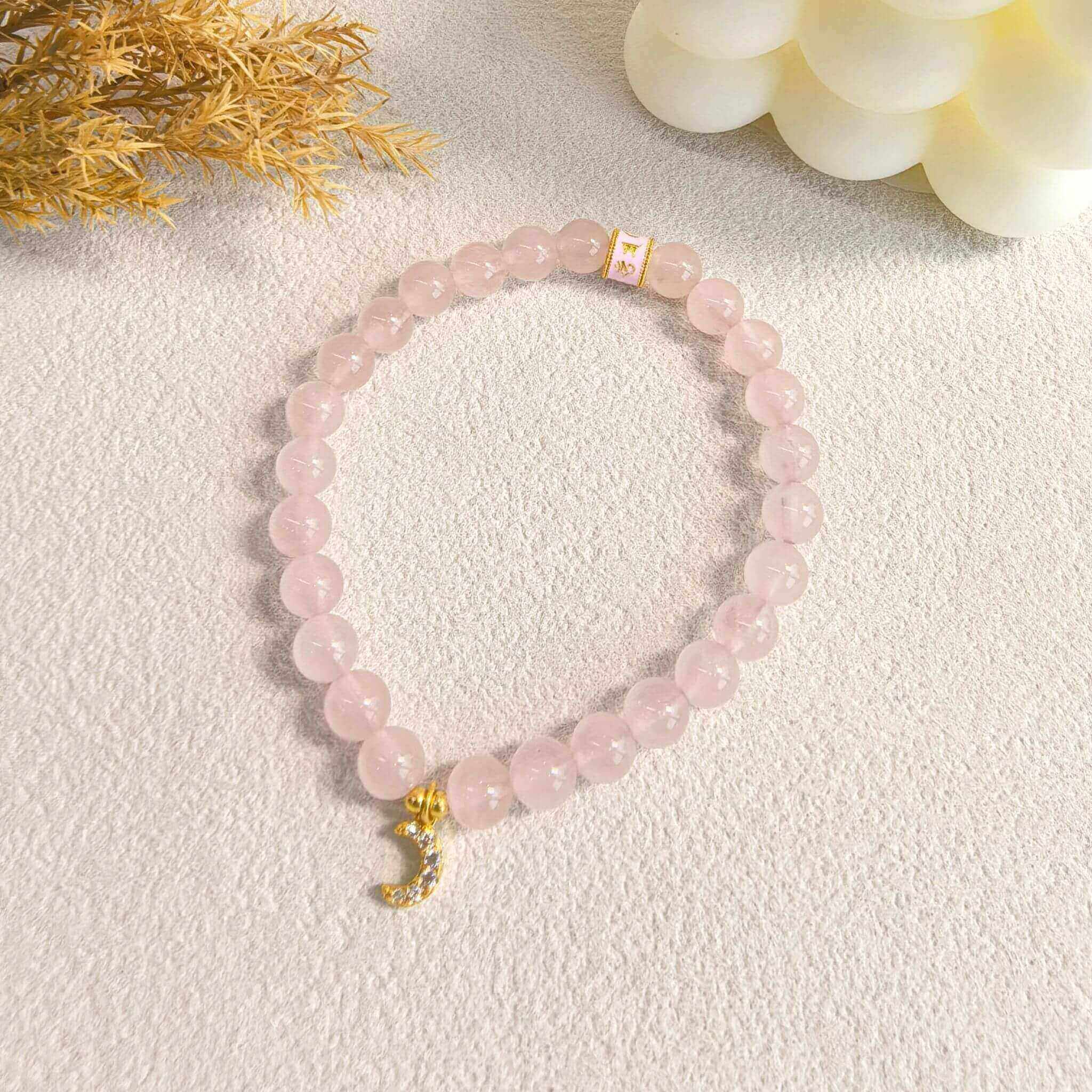 A rose quartz pendant necklace, paired with a crescent-shaped pendant, is elegantly placed on a textured paper, with a soft neutral color as the background.