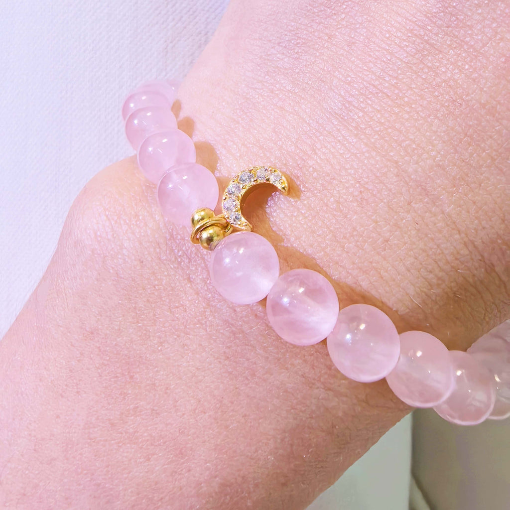 Close up of rose quartz bracelet with sterling silver crescent moon charm on wrist, spiritual crystal jewelry detail.