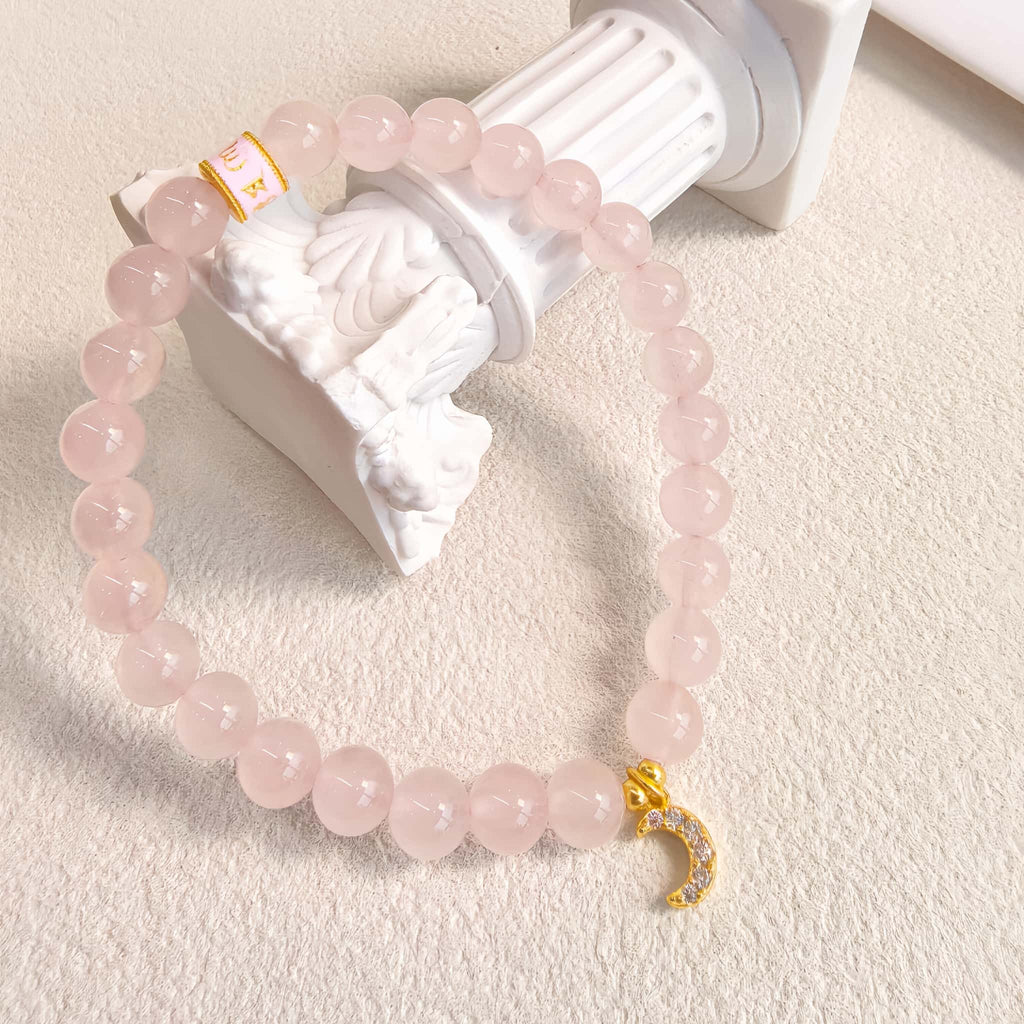 Rose quartz bracelet with moon pendant on vintage plaster column, soft natural light, minimalist style