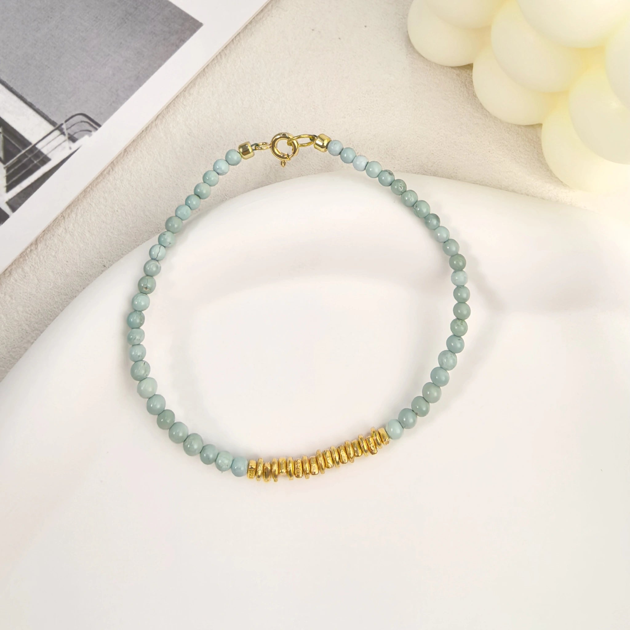 Ins coastal aesthetic flat lay of Calm Tide turquoise chip bracelet with white mermaid tail decor, socean calming beaded bracelet, best gift for her